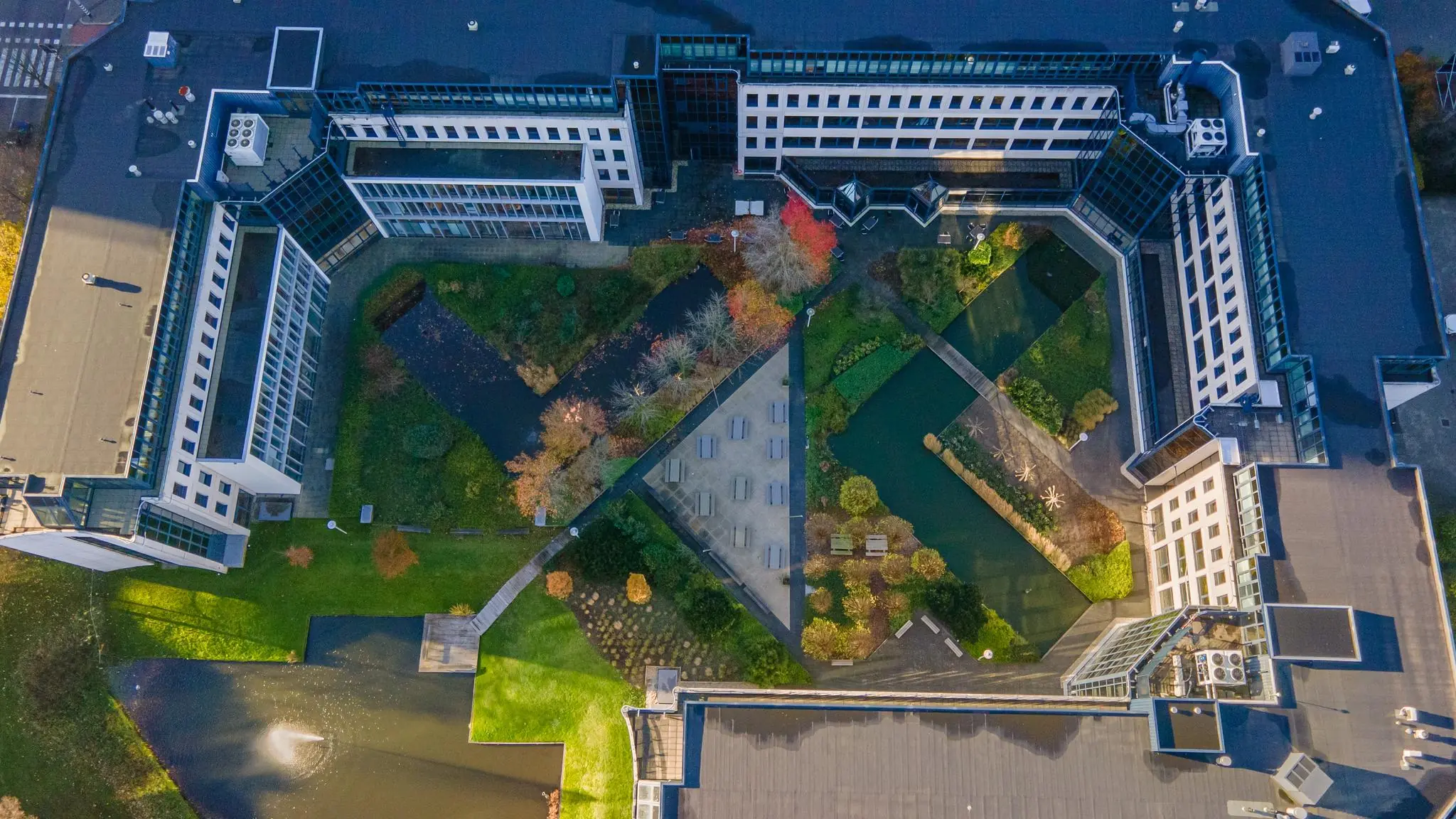 Luchtfoto van een U-vormig kantoorpand aan de De Bruyn Kopsstraat met een groene binnentuin en waterpartijen.